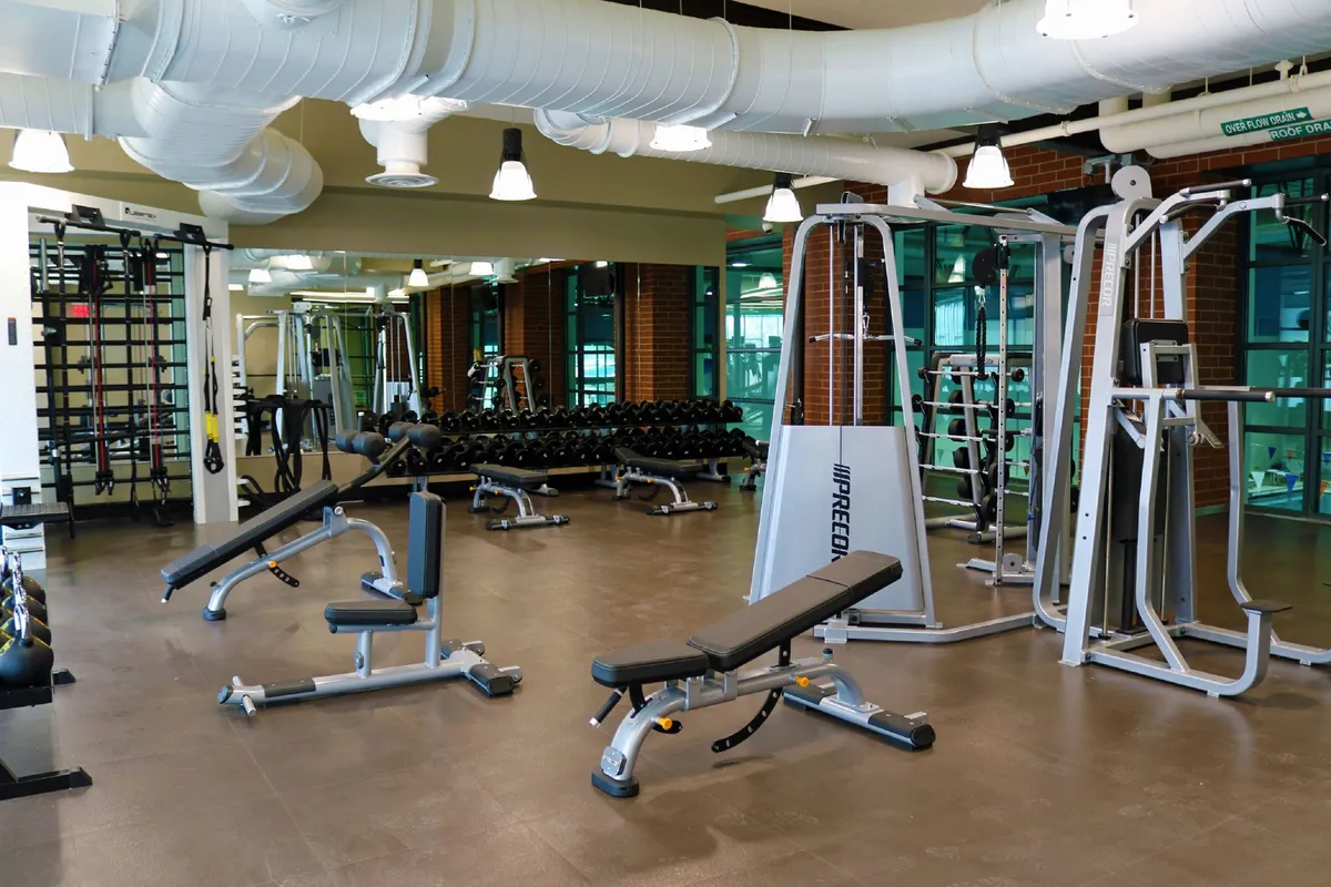 A modern fitness space equipped with weightlifting gear, a large wall mirror, and an open workout area. The mood is energetic, hinting at personal fitness achievements and group exercise opportunities.