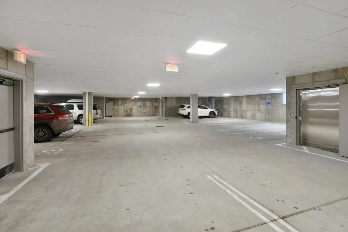 The interior of an underground parking garage with concrete walls, parked vehicles, and modern lighting. The area appears secure and convenient, with easy access for guests coming and going.