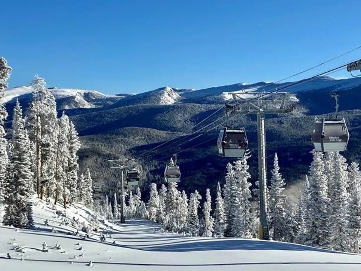 A snow-dusted landscape with a ski lift, snow-covered trees, and a panoramic mountain range under a clear blue sky. The image captures the thrill of winter sports and the serene beauty of the Rockies, suggesting year-round outdoor recreation opportunities.