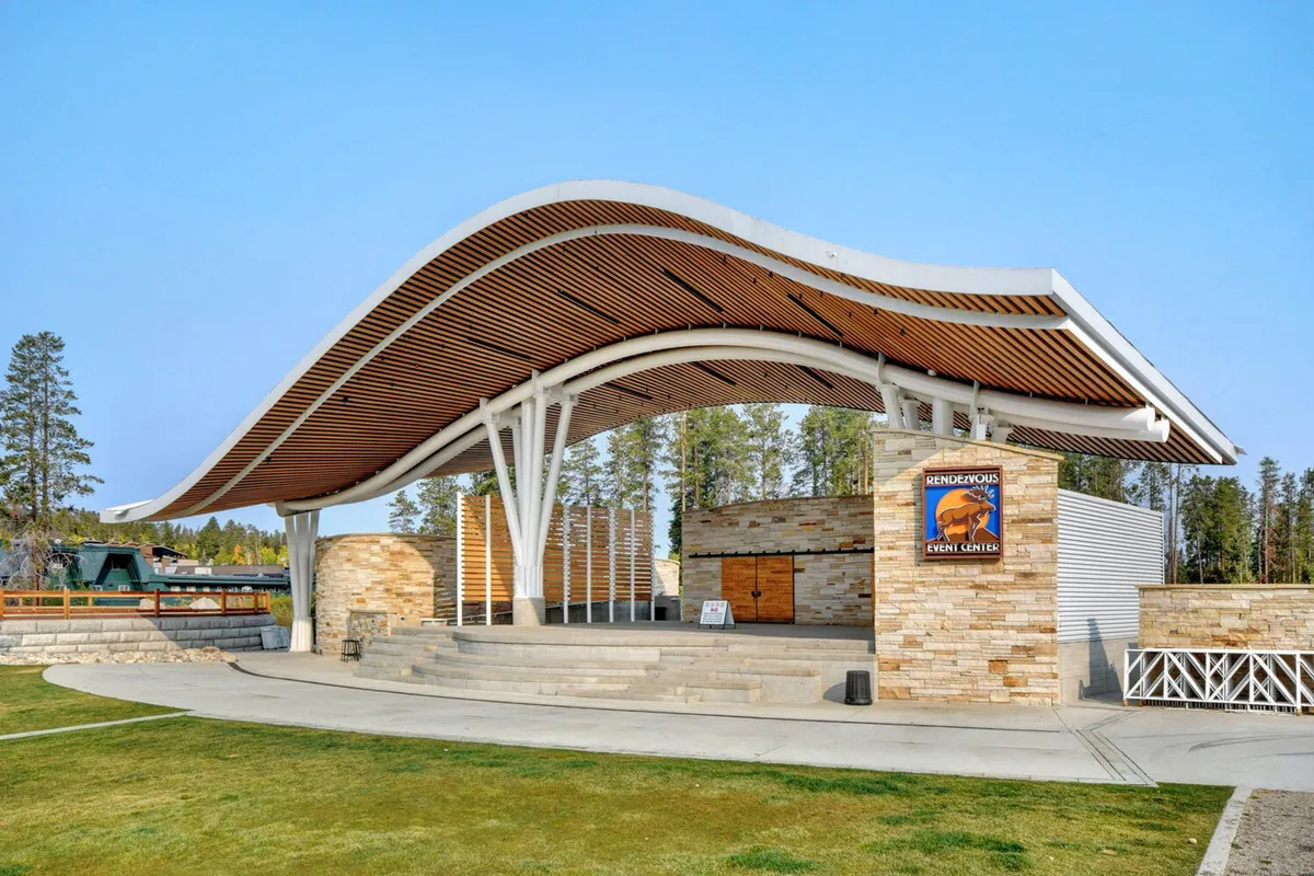 This image captures the distinctive curved roof structure and stone walls of the Hideaway Park Amphitheater. The setting is lively, with a sense of community gatherings and outdoor events, making it clear that this is a hub for local concerts and festivals.