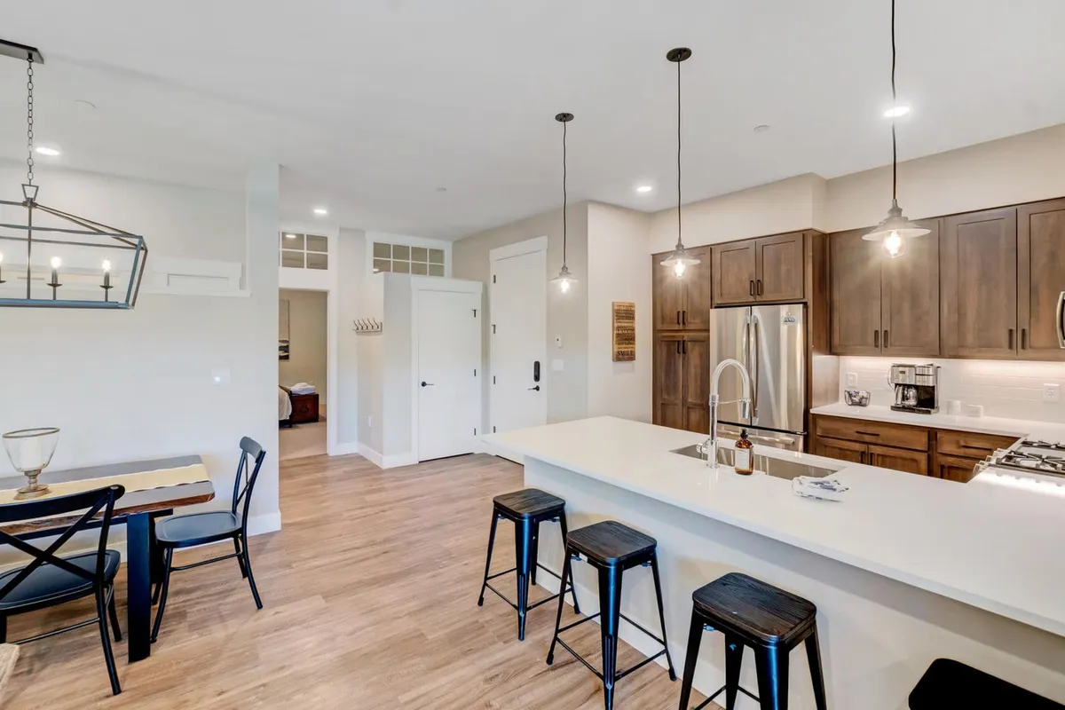 This image spotlights a welcoming open kitchen and dining area, featuring a spacious kitchen island and wooden cabinetry. The scene is set for social gatherings, cooking, and sharing meals, conveying a sense of community and togetherness.