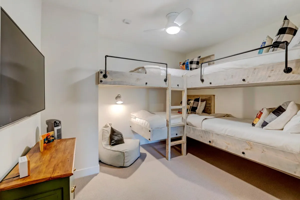 A playful bunk room featuring two sets of wooden bunk beds, a television, and a small wooden table—ideal for kids or adventurous adults. The room is bright and inviting, designed for fun sleepovers or movie nights.