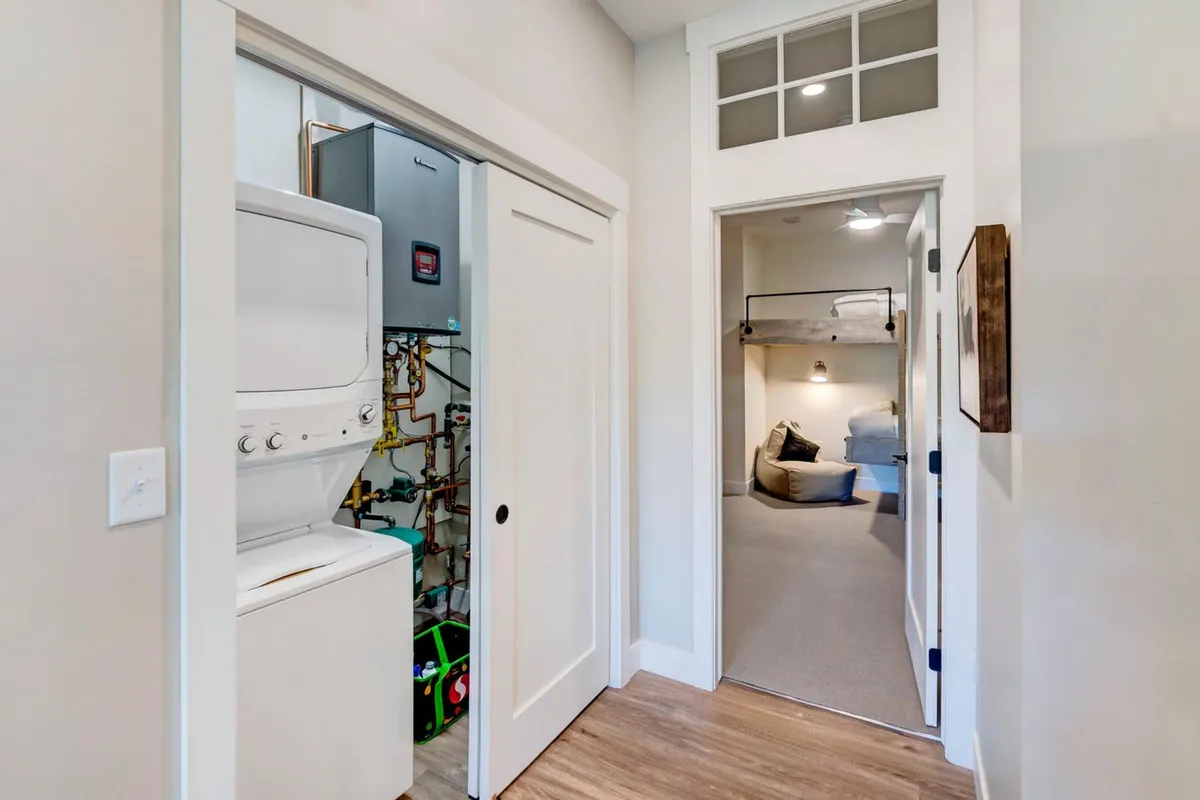 A compact laundry area featuring stacked washer and dryer units, with a glimpse of a cozy bedroom through the doorway. The space is functional yet inviting, hinting at thoughtful conveniences for longer or more comfortable stays.