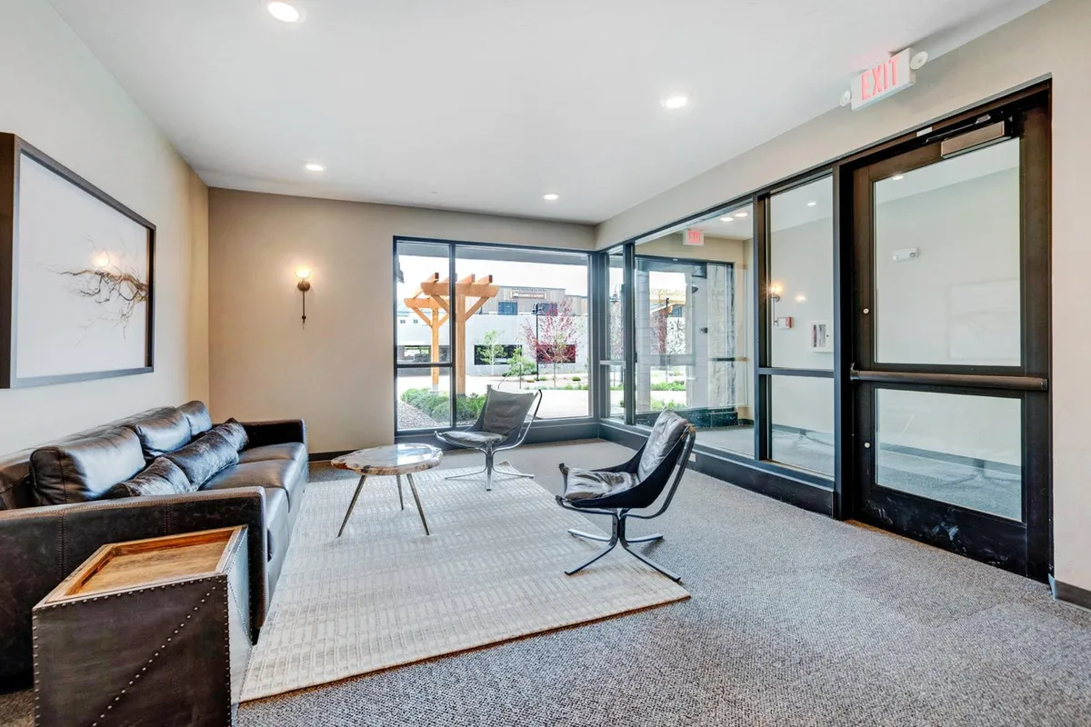 This bright living space features a comfortable sofa and armchairs arranged around a coffee table, positioned near floor-to-ceiling windows that bring the outdoors in. The layout is perfect for casual conversations, socializing, or simply relaxing and enjoying the morning light.